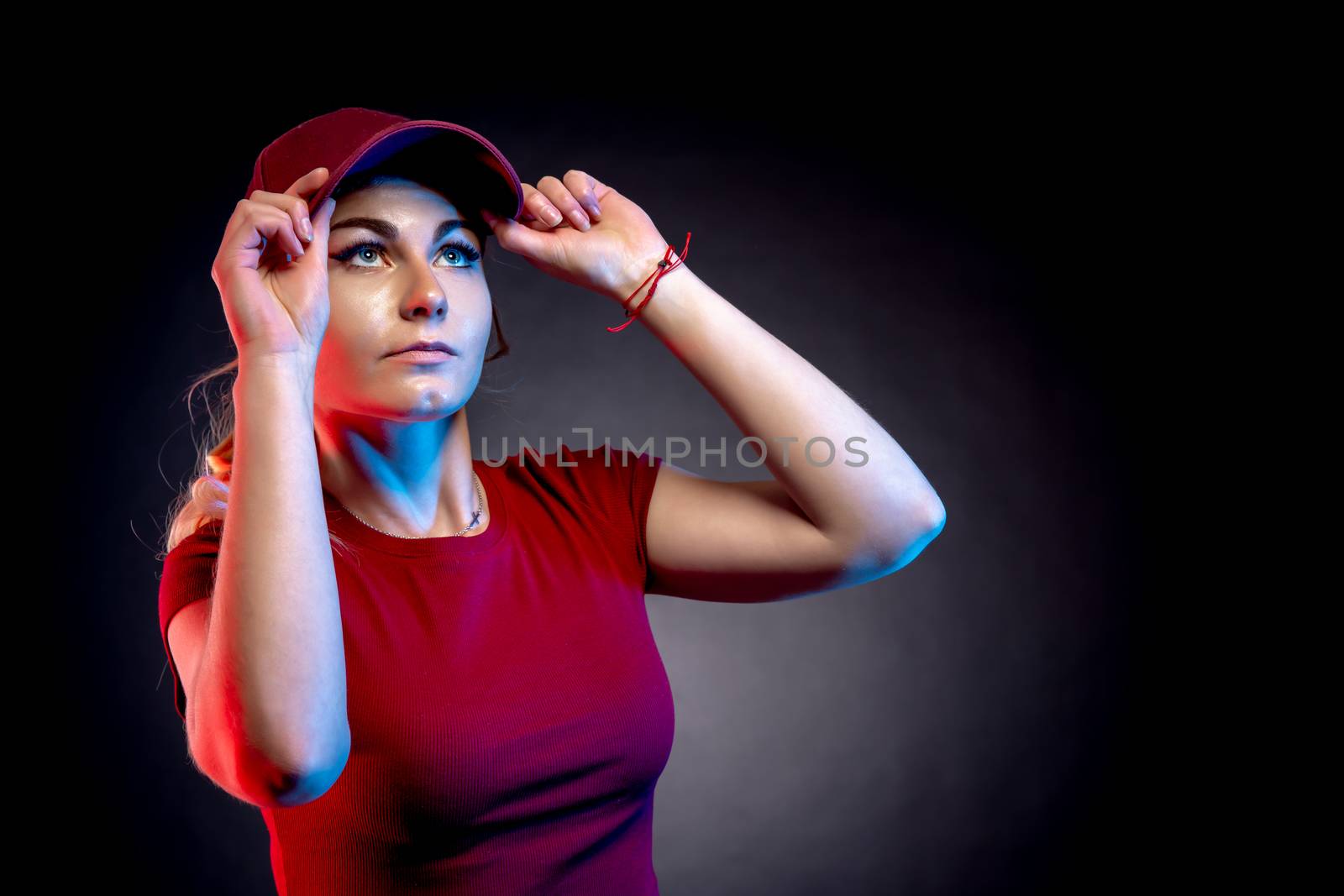 Portrait of a woman in a baseball cap on a black background. red and blue color illuminates the figure by Edophoto
