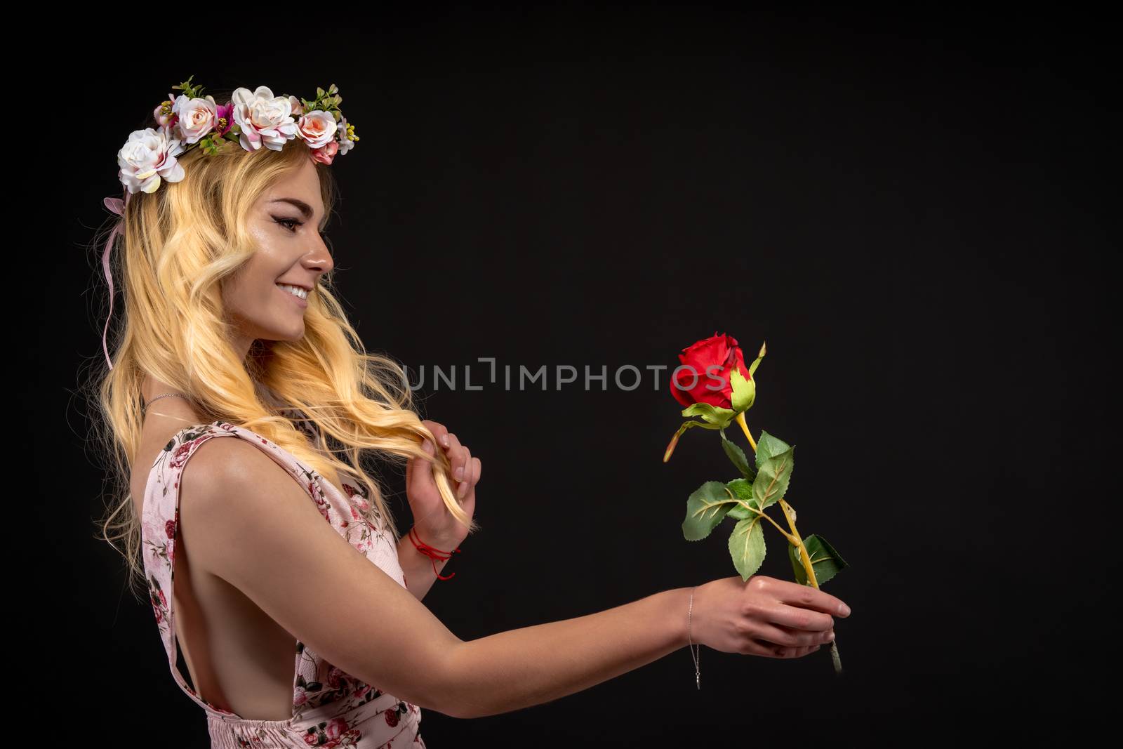 portrait of a young woman in a dress on a black background with a floral wreath on her head. she brought a red rose in her hand. copy space by Edophoto