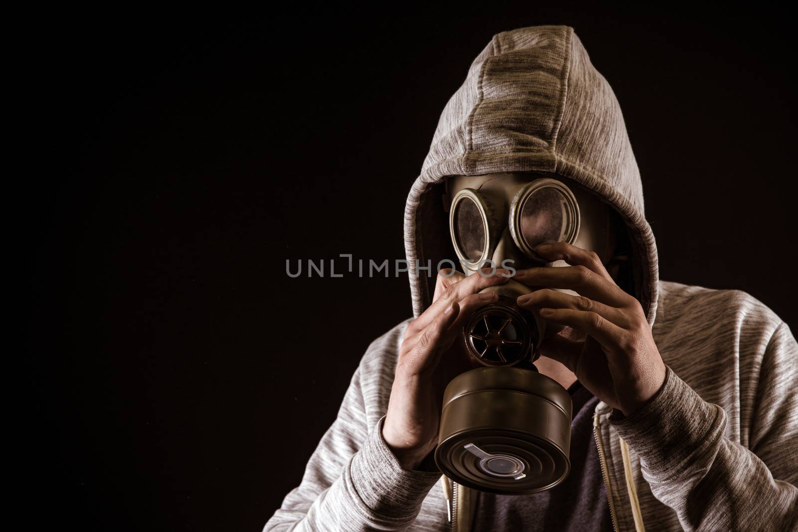 man puts on gas mask to protect against gas. Portrait on black background, dramatic coloring.