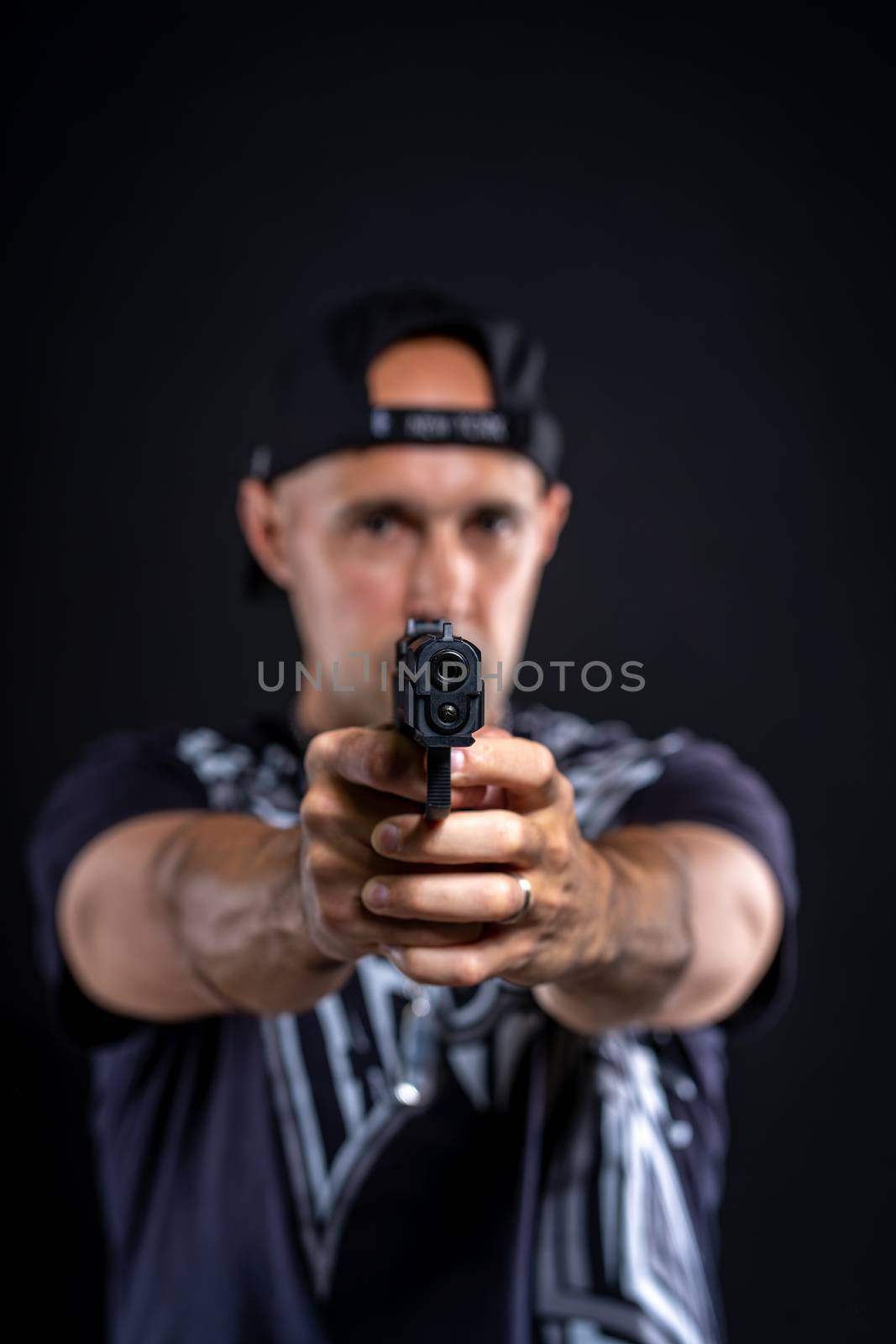 man pointing gun at object, portrait on black background.