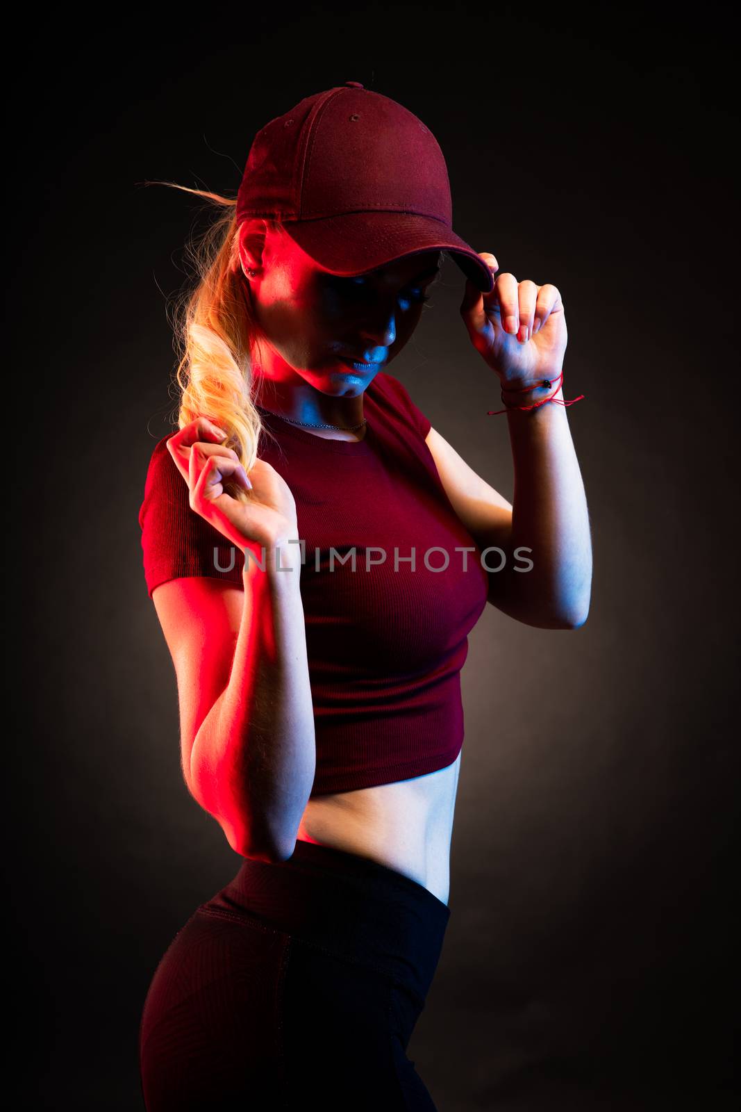 Portrait of a woman in a baseball cap on a black background. red and blue color illuminates the figure by Edophoto