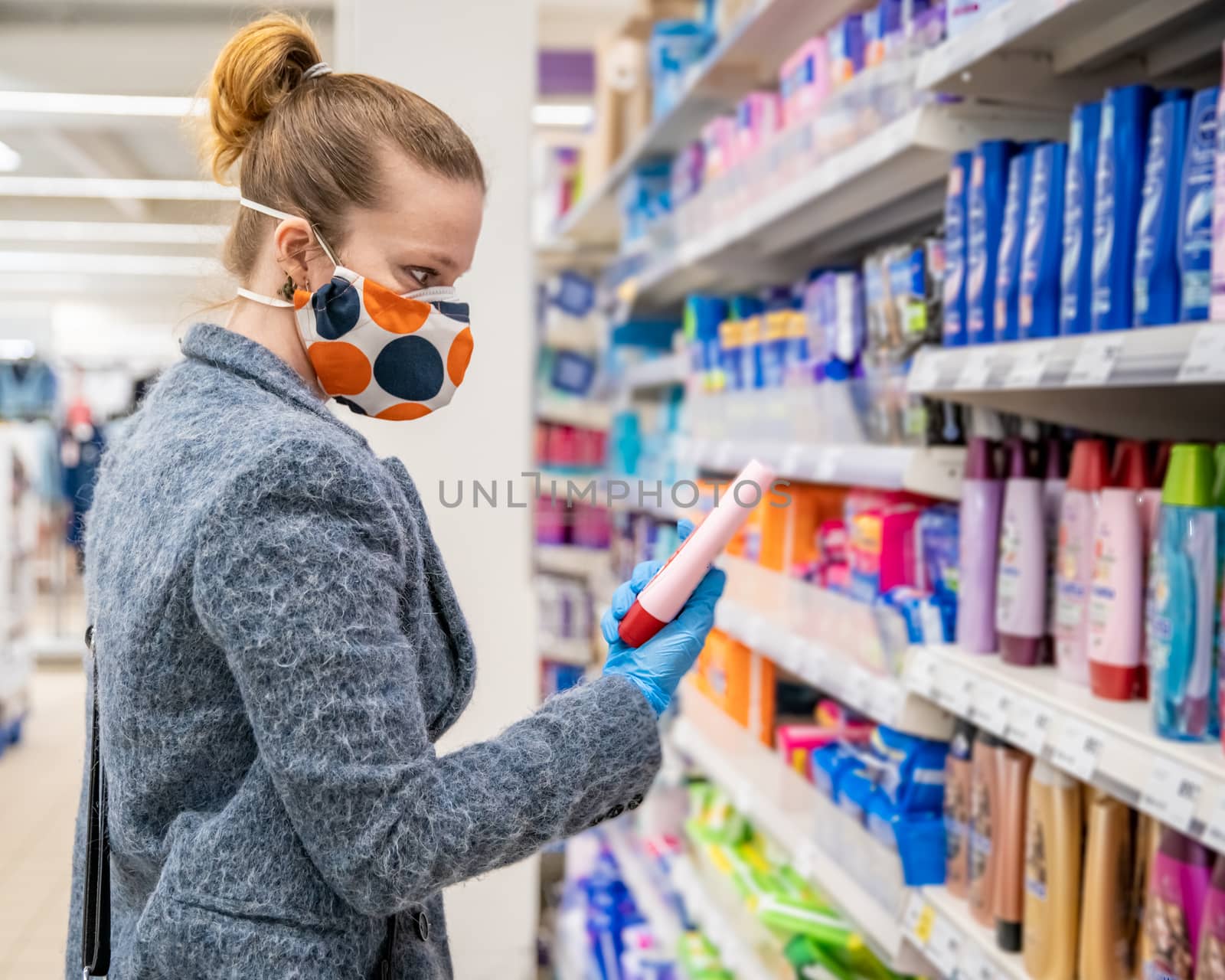 woman buying cosmetics in a shopping center with a health mask on her face during a coronavirus epidemic by Edophoto