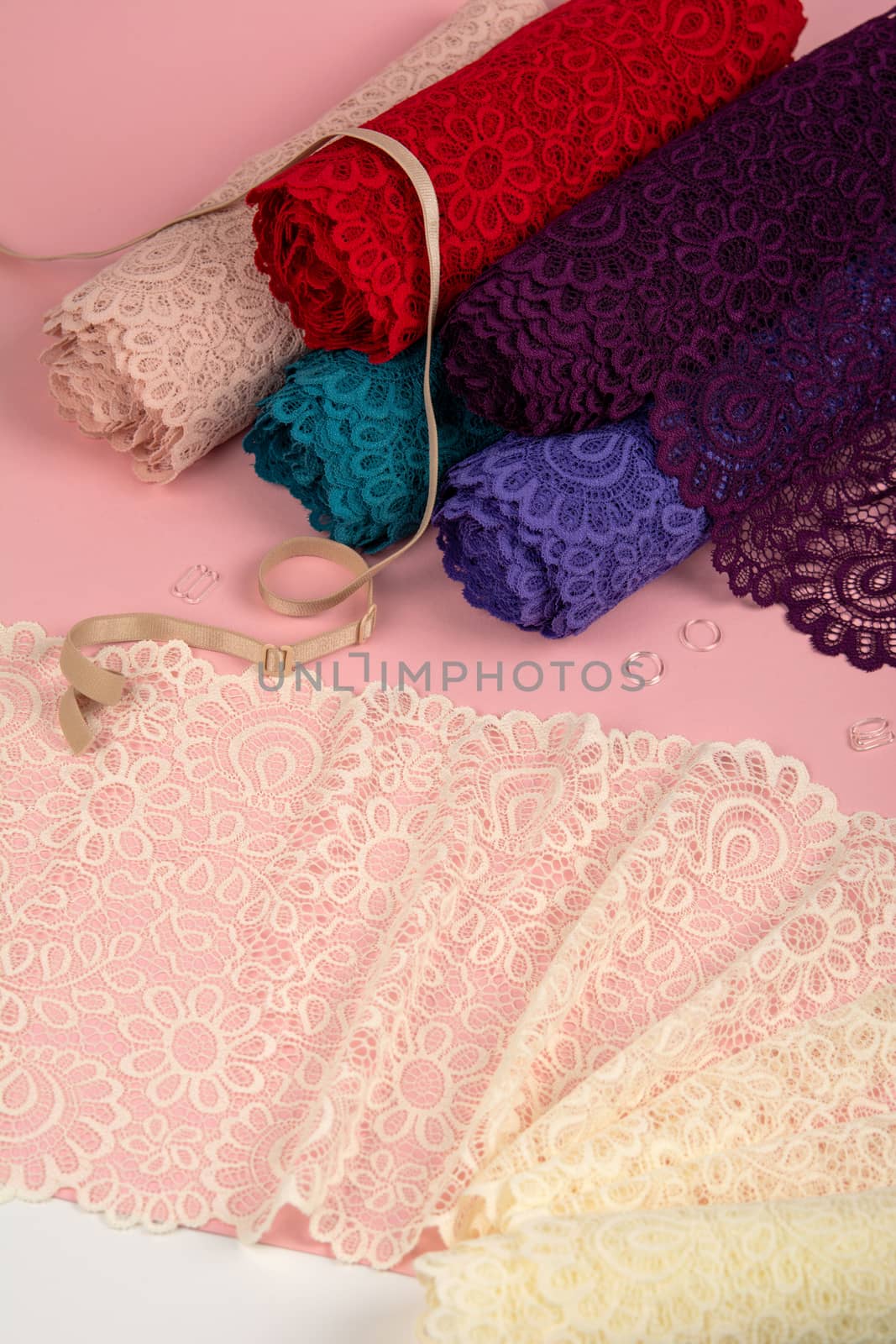 Roll of Delicate color laces for panties and bras on pink background with plastic fittings. Elastic material. Using for Atelier and fabric store.