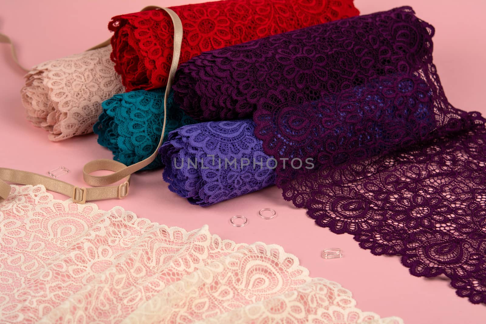 Roll of Delicate color laces for panties and bras on pink background with plastic fittings. Elastic material. Using for Atelier and fabric store.