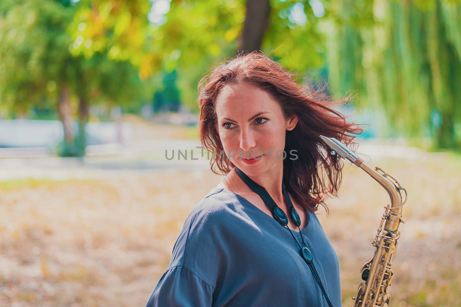 Close portrait of a young red-haired woman in a green park with a saxophone by chernobrovin
