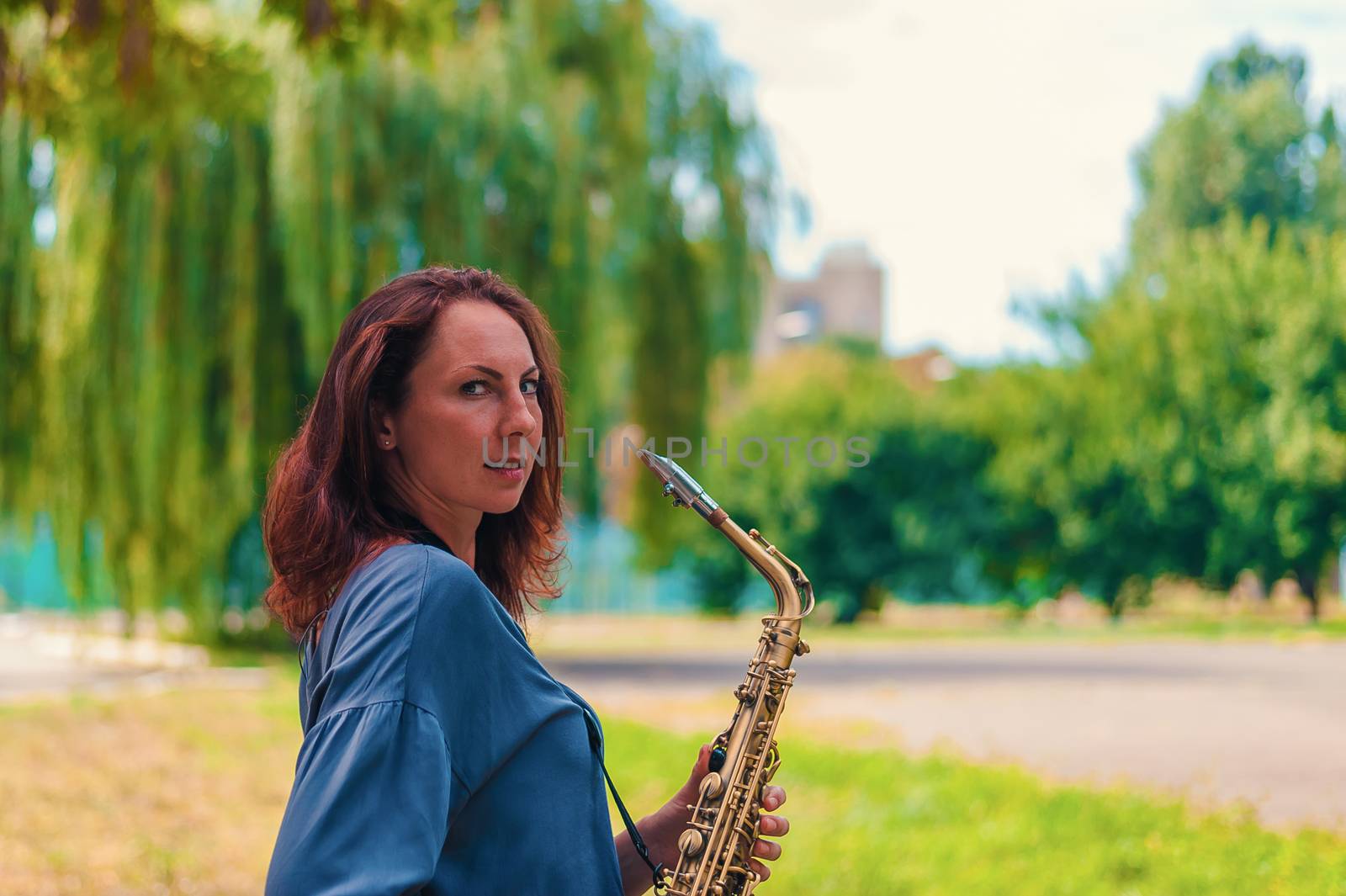 cute young redhead woman posing with saxophone in city park