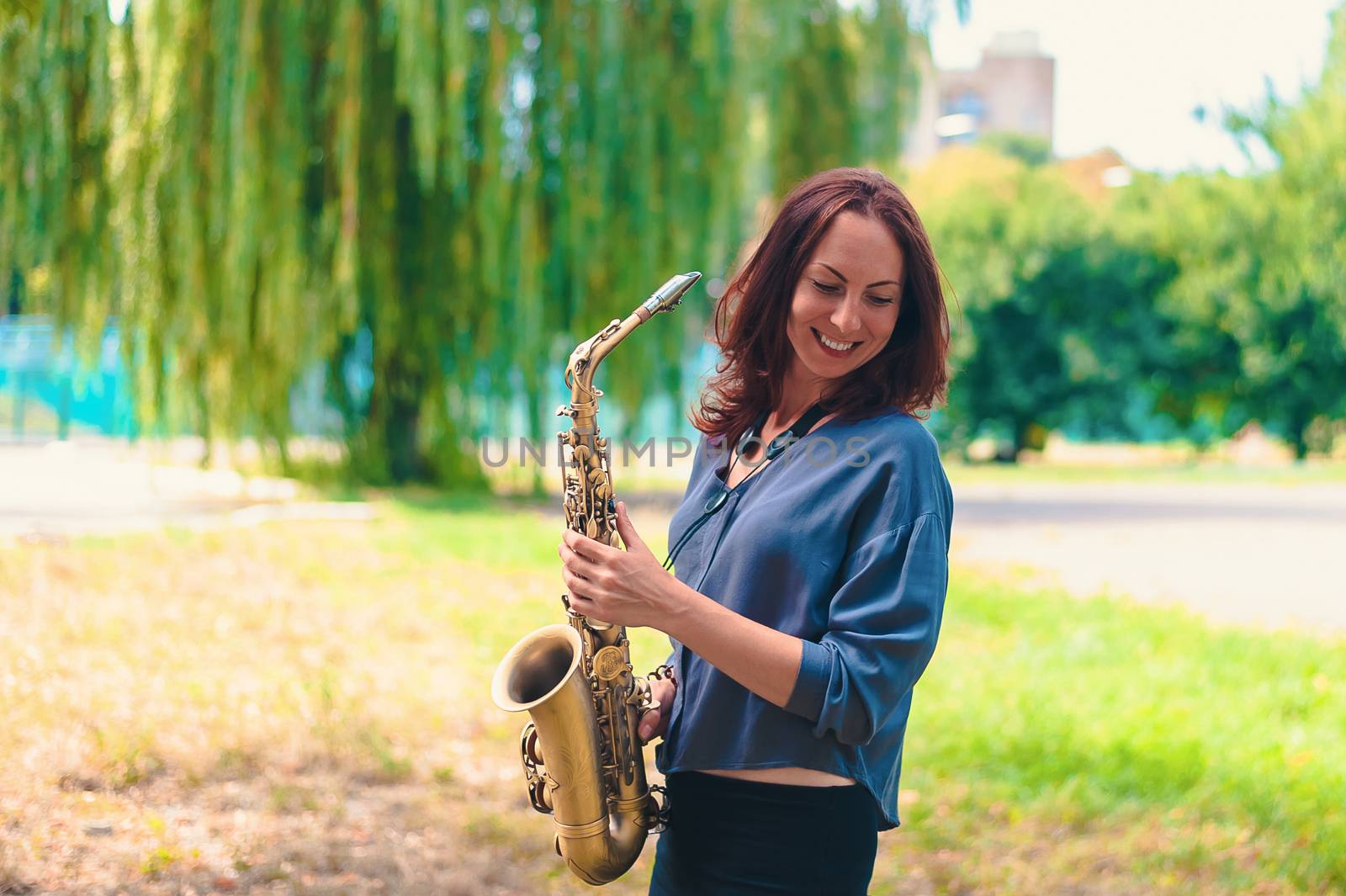 lovely girl with red hair holds a saxophone in her hands and laughs in nature