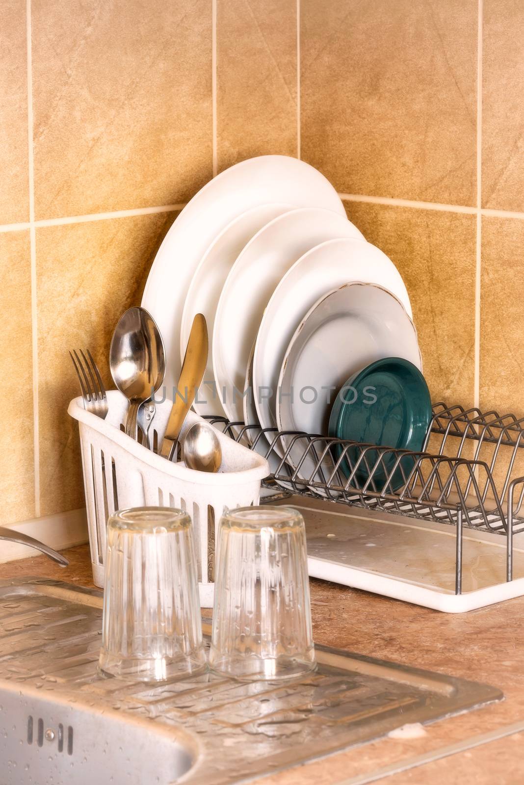 Washed plates, cutlery and glasses, drying in their racks close to the sink in the kitchen