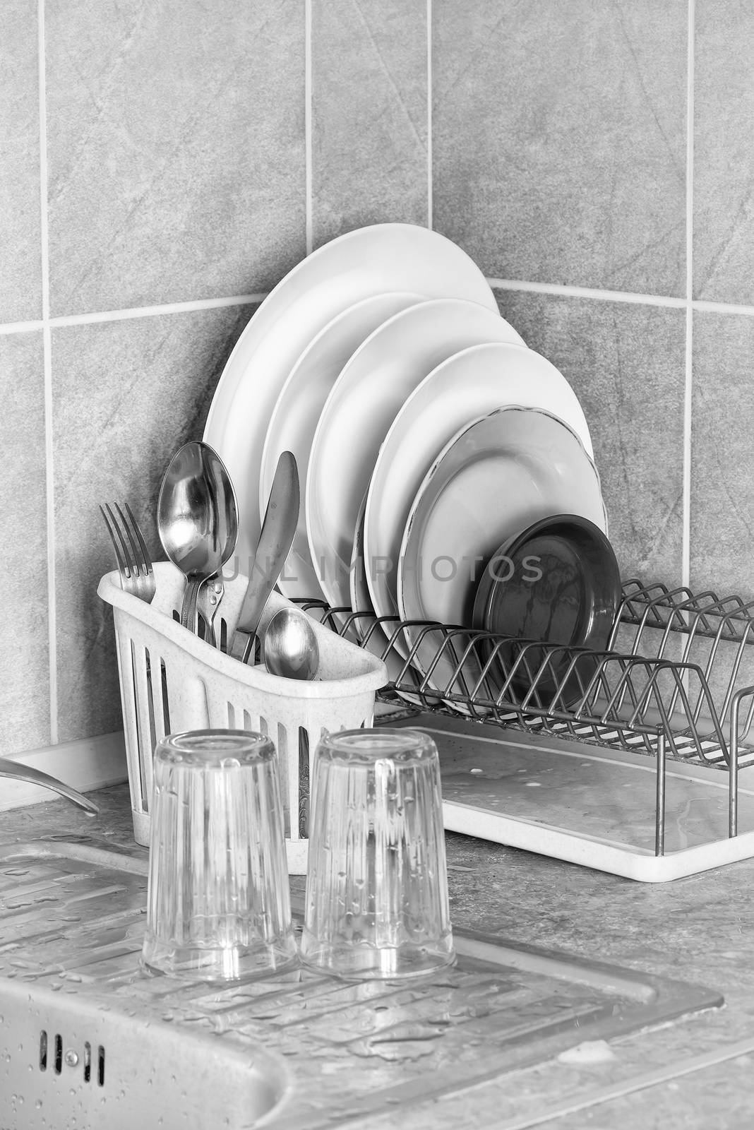 Washed plates, cutlery and glasses, drying in their racks close to the sink in the kitchen