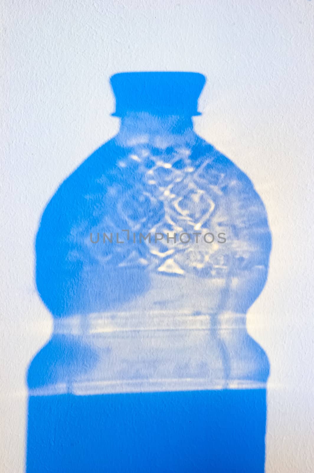 Projection of the transparent shadow of an empty plastic bottle of water on a white wall