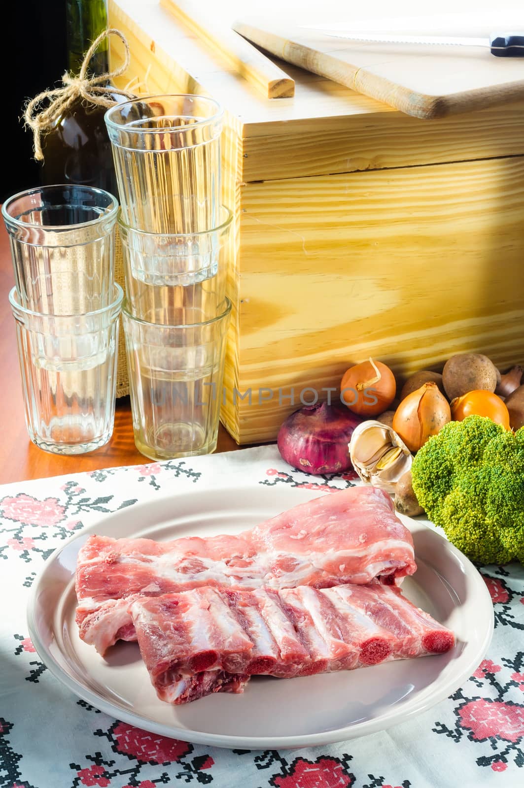 Pork ribs on a plate, rustic ambience around, with vegetable, glasses and bottle
