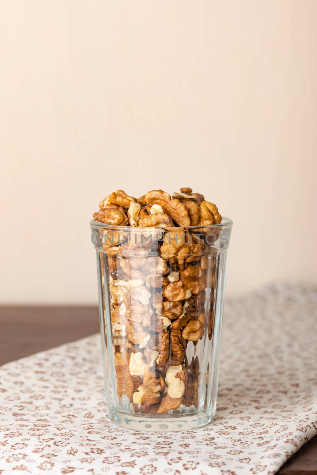 Fresh peeled walnuts in a glass on a wooden table with a white flowery tablecloth, and negative space for copy text