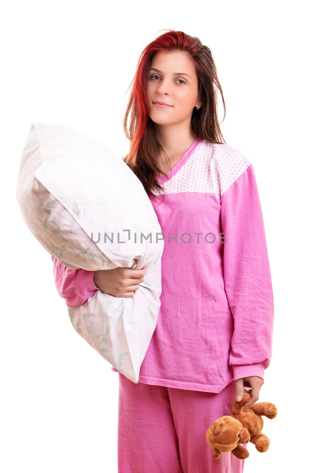 Beautiful smiling young girl in pink pajamas holding a pillow and a teddy bear, preparing to go to sleep, isolated on white background. Sleep and relaxation concept.
