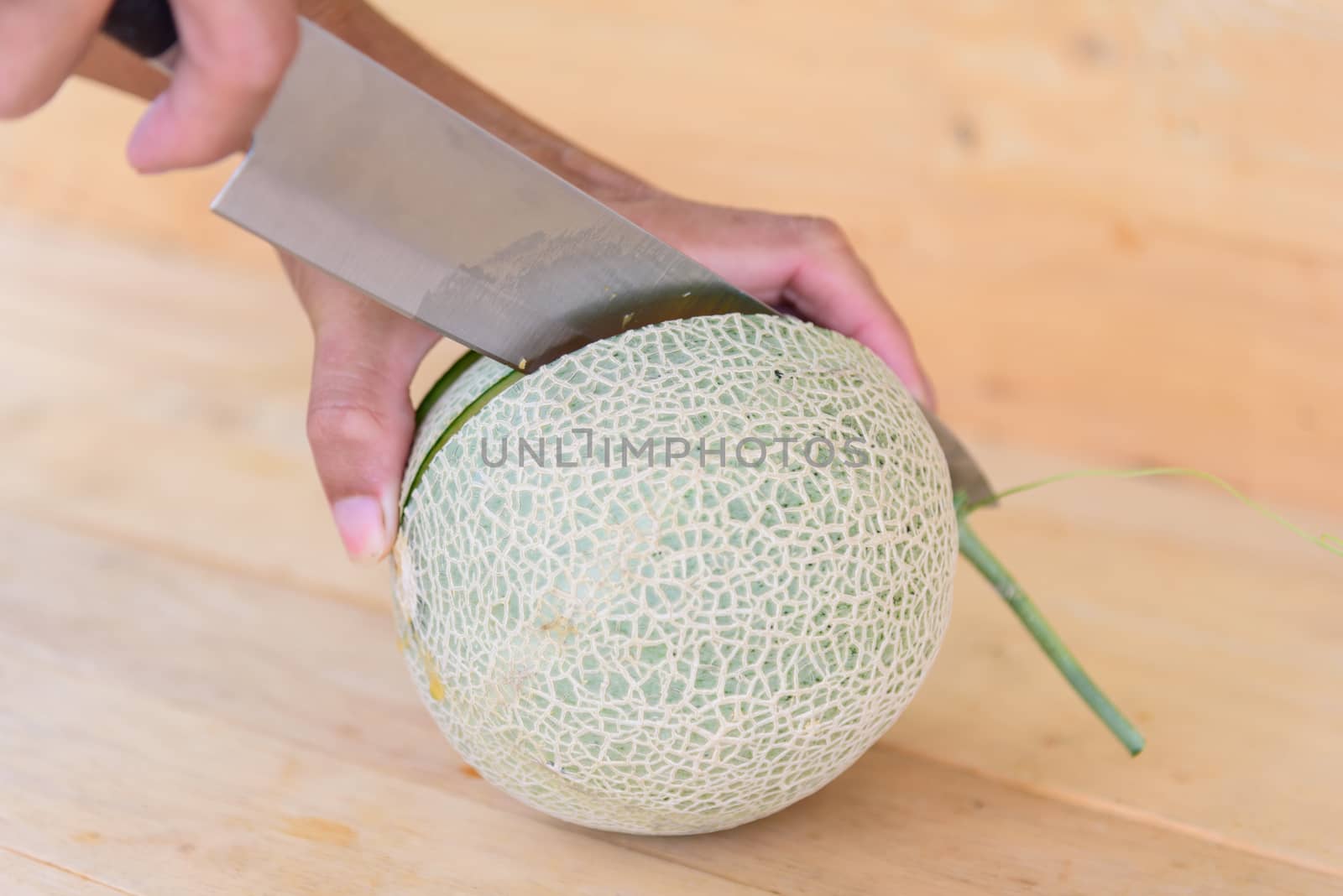 The man use knife split the orange melon on wood plate