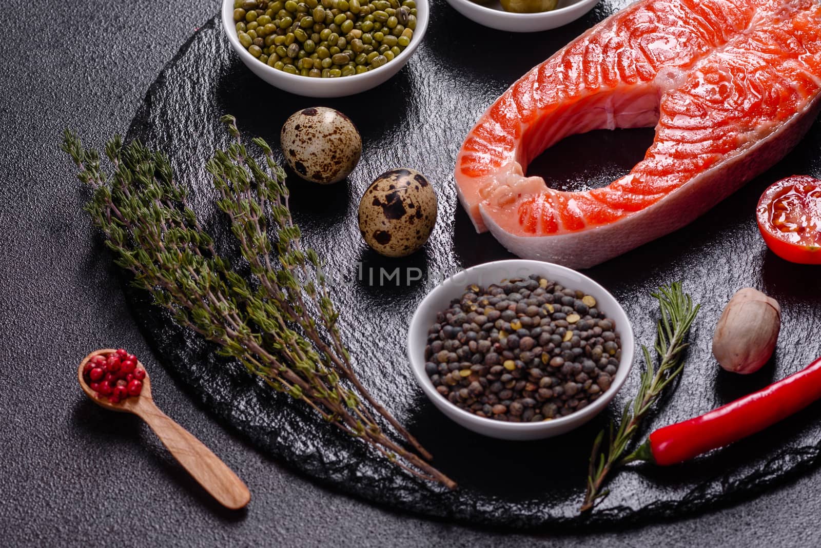 Raw trout red fish steak served with herbs and lemon and olive oil on a dark background. Cooking Salmon, sea food. Healthy eating concept