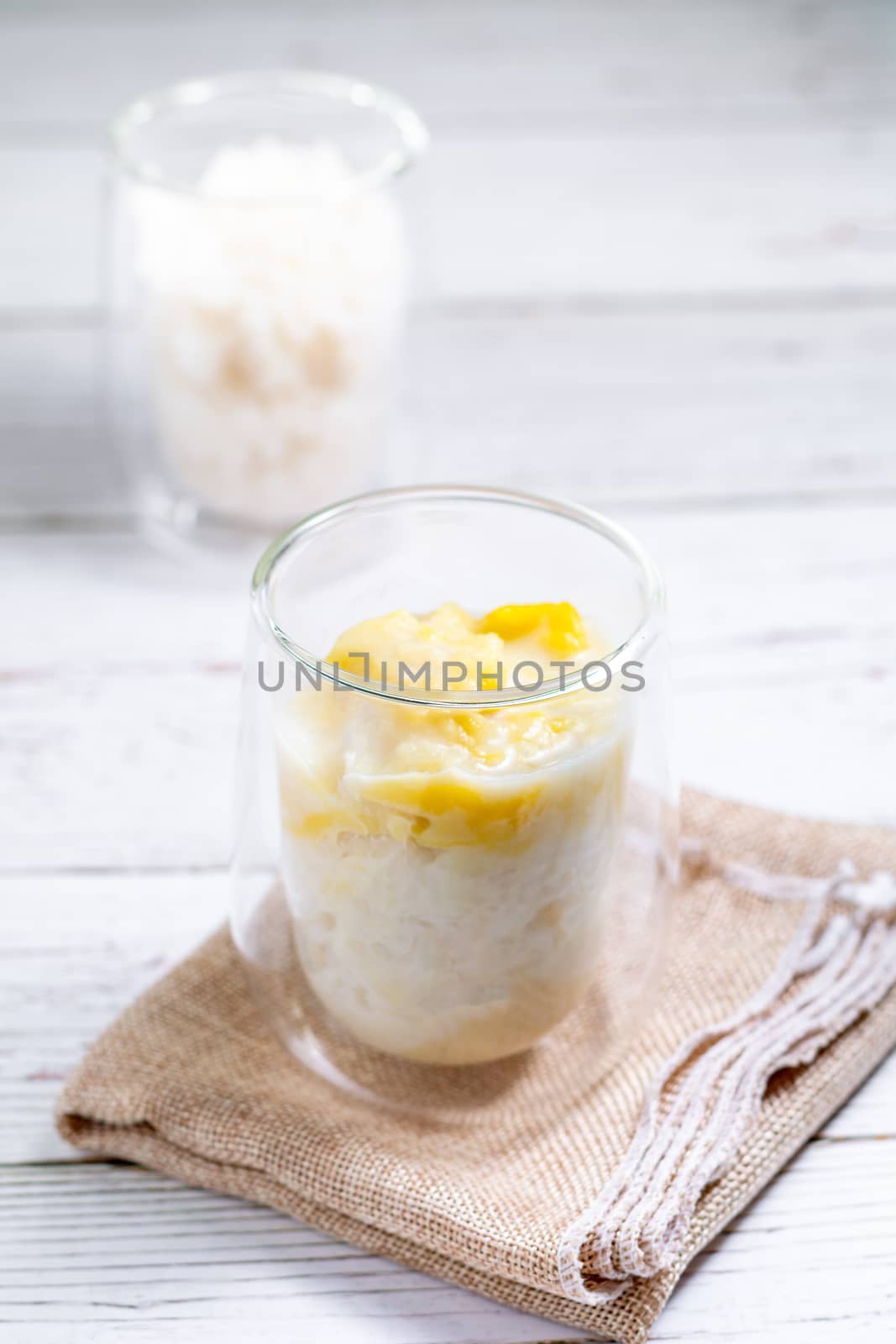 Summer appetizer of Thailand concept. Durian and sticky rice with coconut milk cream in transparent glass on white wooden table and brown table cloth. Famous street food in Thailand.  