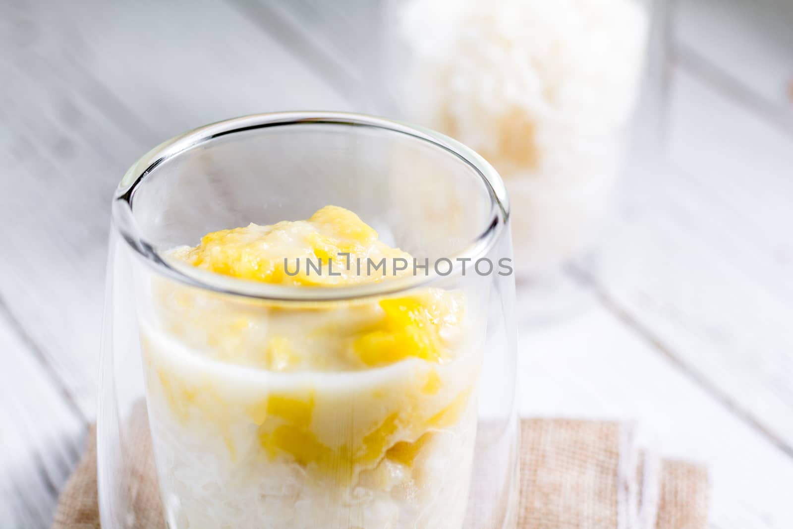 Summer appetizer of Thailand concept. Durian and sticky rice with coconut milk cream in transparent glass on white wooden table and brown table cloth. Famous street food in Thailand.  