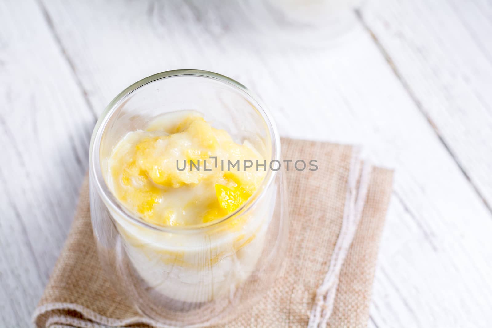 Summer appetizer of Thailand concept. Durian and sticky rice with coconut milk cream in transparent glass on white wooden table and brown table cloth. Famous street food in Thailand.  