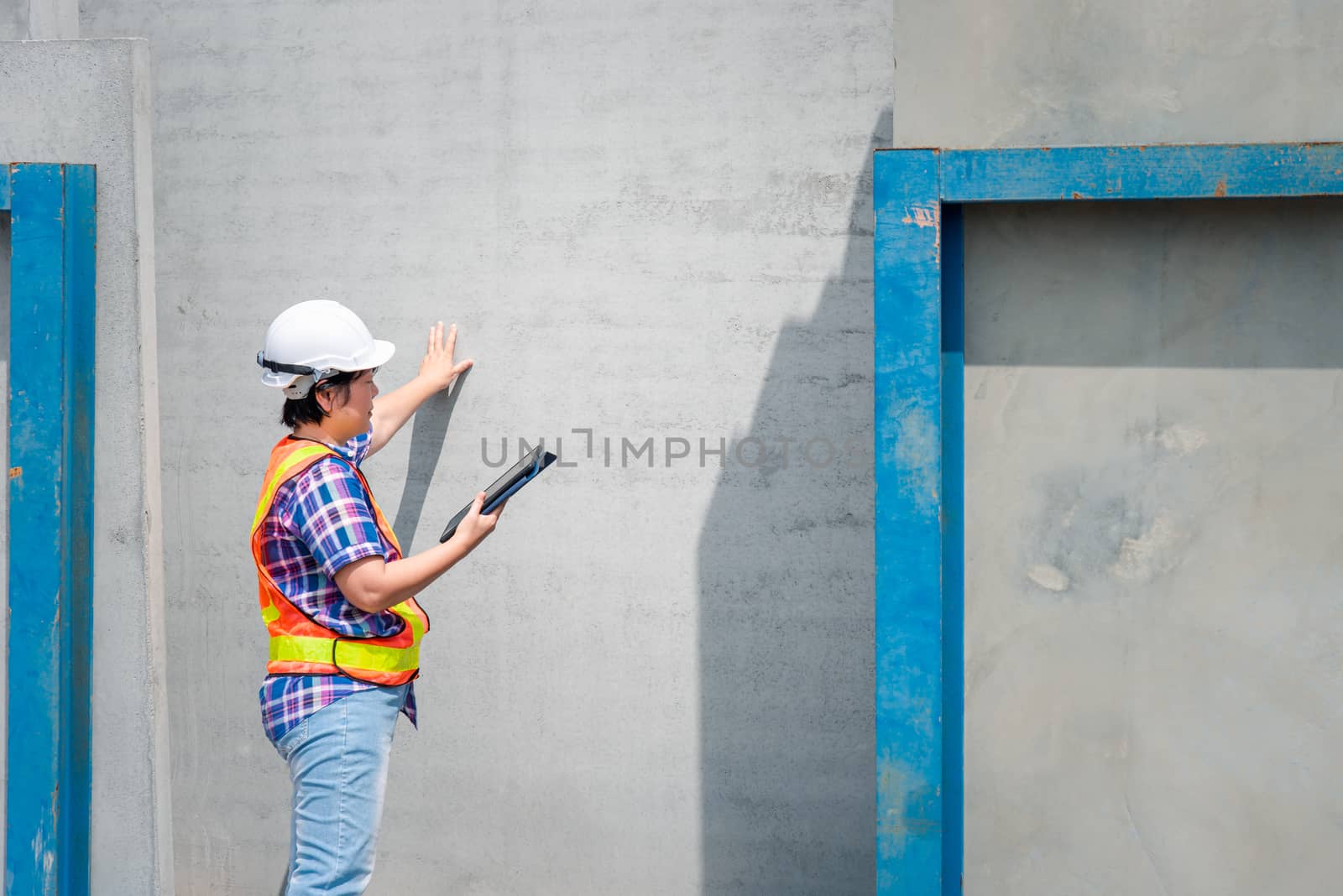 Asian woman civil construction engineer worker or architect with helmet and safety vest working and holding a touchless tablet computer for see blueprints or plan at a building or construction site