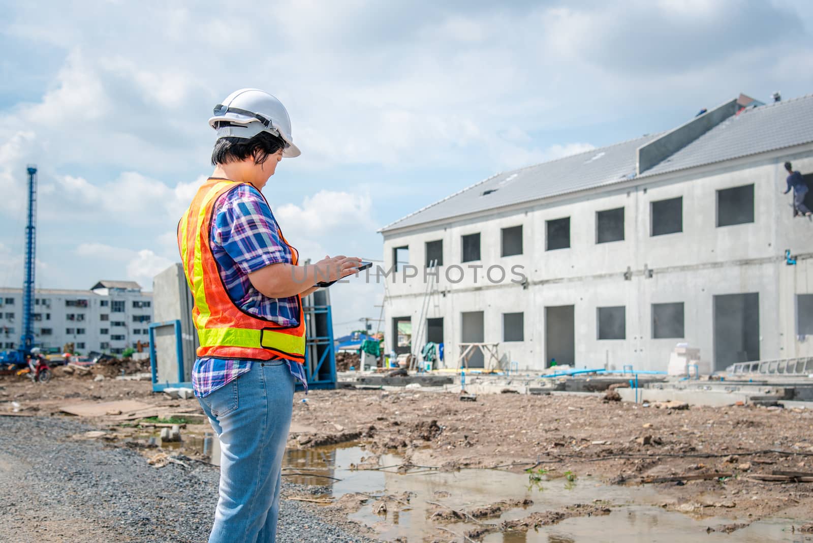 Asian woman civil construction engineer worker or architect with helmet and safety vest working and holding a touchless tablet computer for see blueprints or plan at a building or construction site
