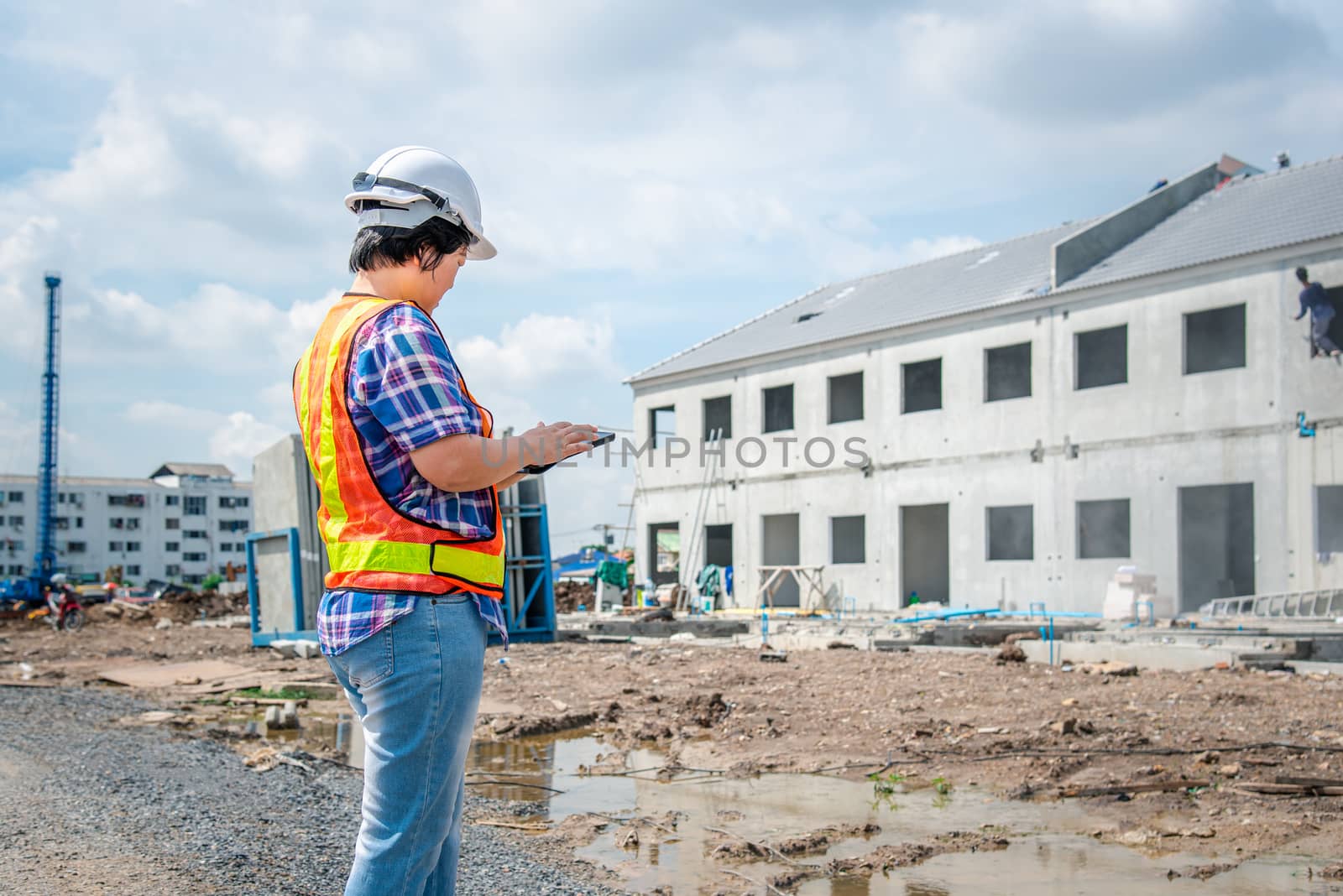 Asian woman civil construction engineer worker or architect with helmet and safety vest working and holding a touchless tablet computer for see blueprints or plan at a building or construction site