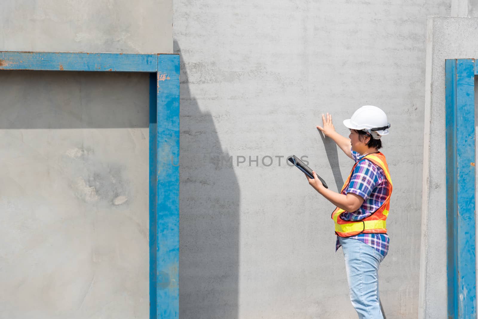 Asian woman civil construction engineer worker or architect with helmet and safety vest working and holding a touchless tablet computer for see blueprints or plan at a building or construction site