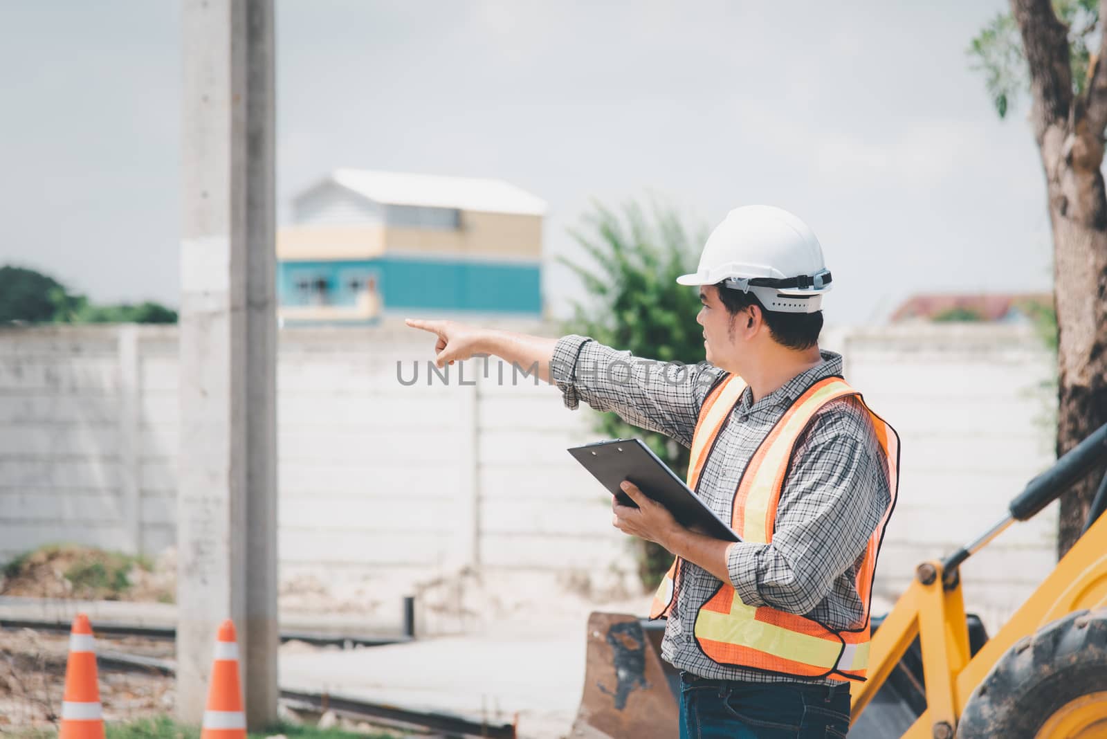 Asian man civil construction engineer worker or architect with helmet and safety vest working and holding a touchless tablet computer for see blueprints or plan at a building or construction site