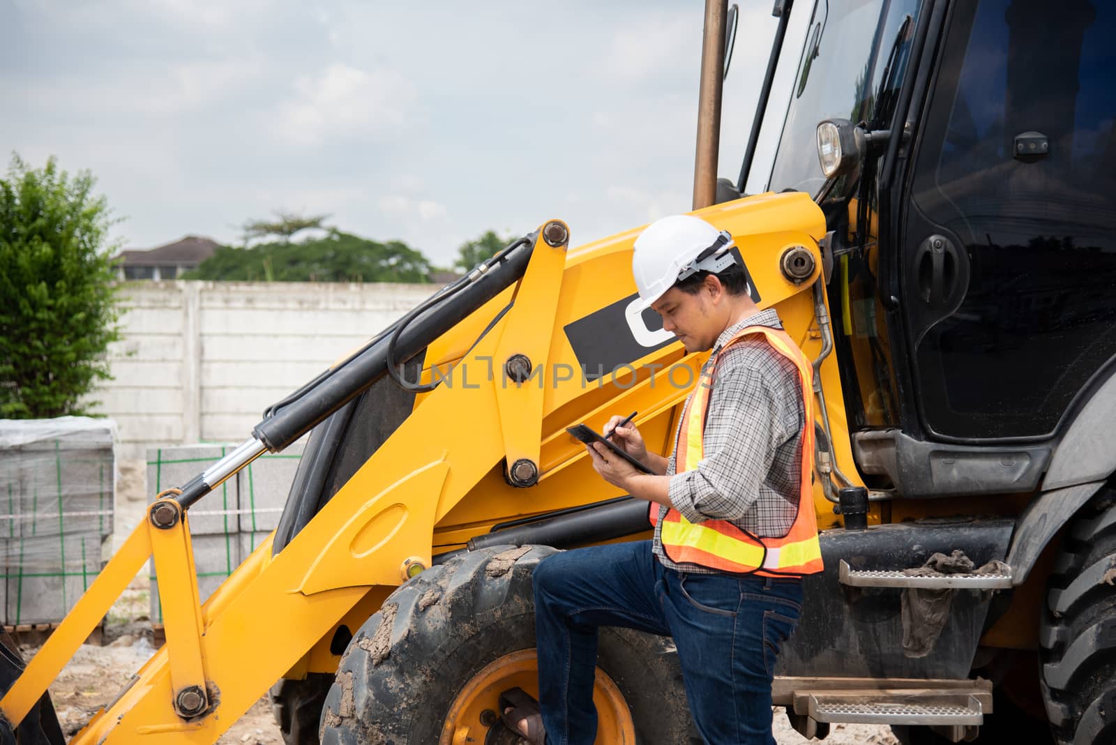 Asian man civil construction engineer worker or architect with helmet and safety vest working and holding a touchless tablet computer for see blueprints or plan at a building or construction site