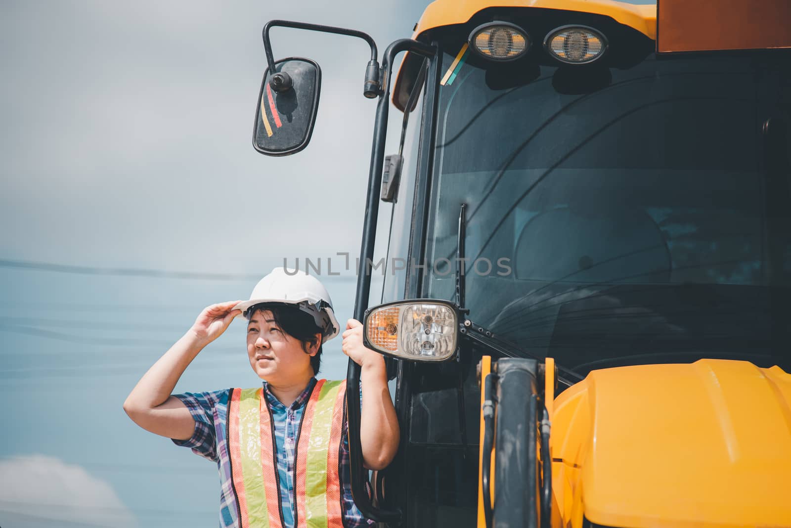 Asian woman civil construction engineer worker or architect with helmet and safety vest happy working and loader backhoe at a building or construction site