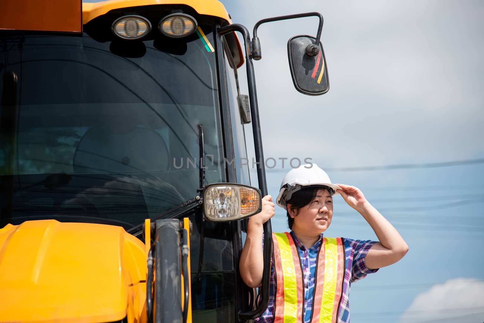 Asian woman civil construction engineer worker or architect with helmet and safety vest happy working and loader backhoe at a building or construction site