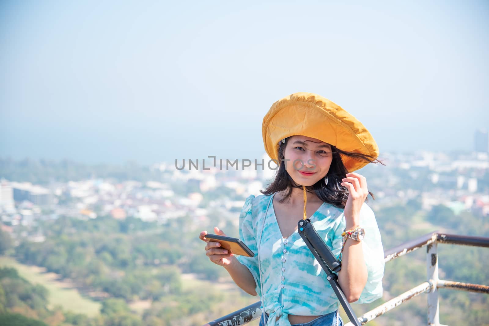 Asian pretty cute woman with hat relax and use smartphone at seaside city landscape viewpoint on mountain with happy and freedom emotion in concept travel, vacation, leisure in life