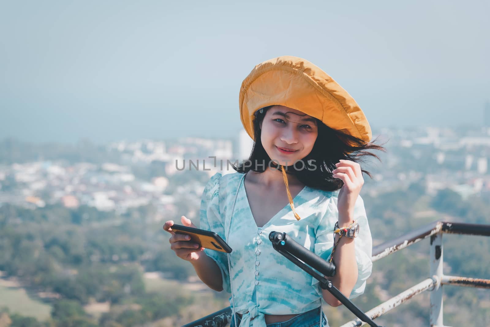 Asian pretty cute woman with hat relax and use smartphone at seaside city landscape viewpoint on mountain with happy and freedom emotion in concept travel, vacation, leisure in life