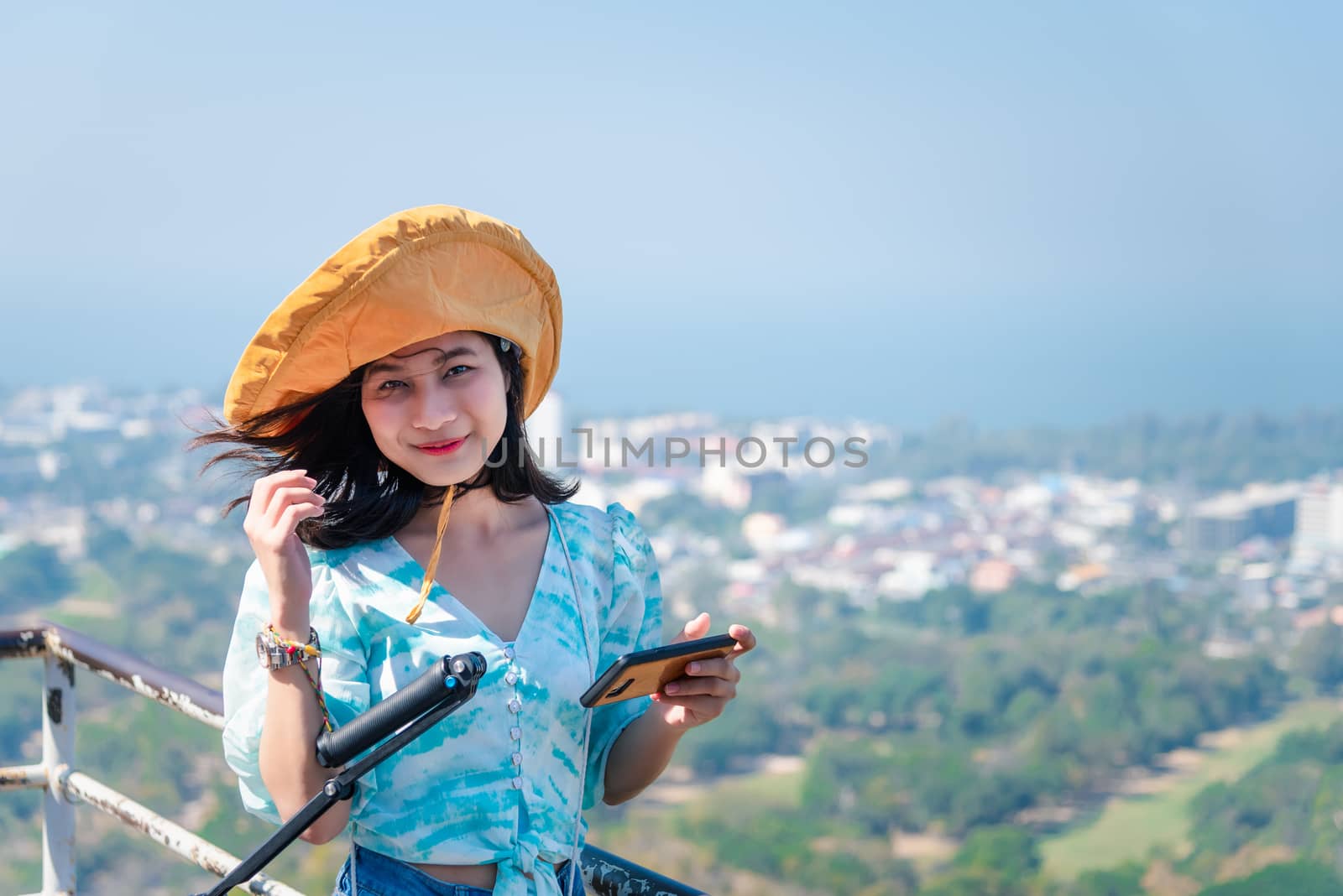 Asian pretty cute woman with hat relax and use smartphone at seaside city landscape viewpoint on mountain with happy and freedom emotion in concept travel, vacation, leisure in life