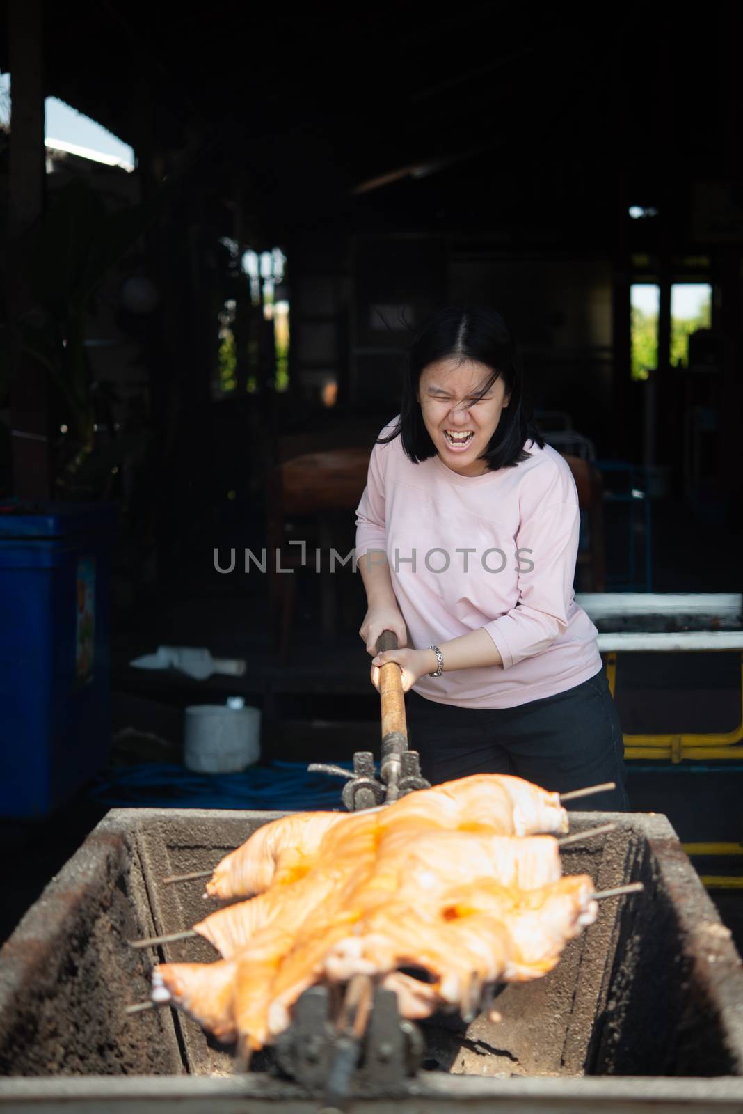 Asian woman chef cooking Barbecued Suckling Pig by roasting pork on charcoal for sale at Thai street food market or restaurant in Thailand