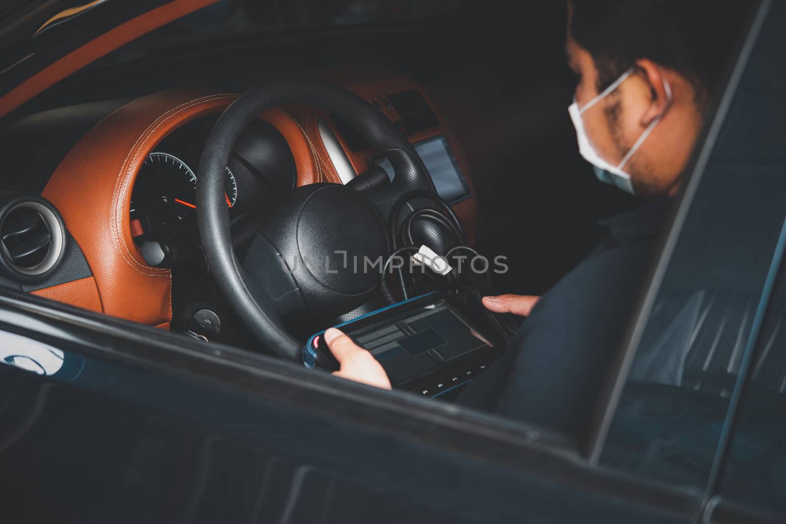 Car mechanic or serviceman checking a car engine by OBD-II electric tools for fix and repair problem at car garage or repair shop