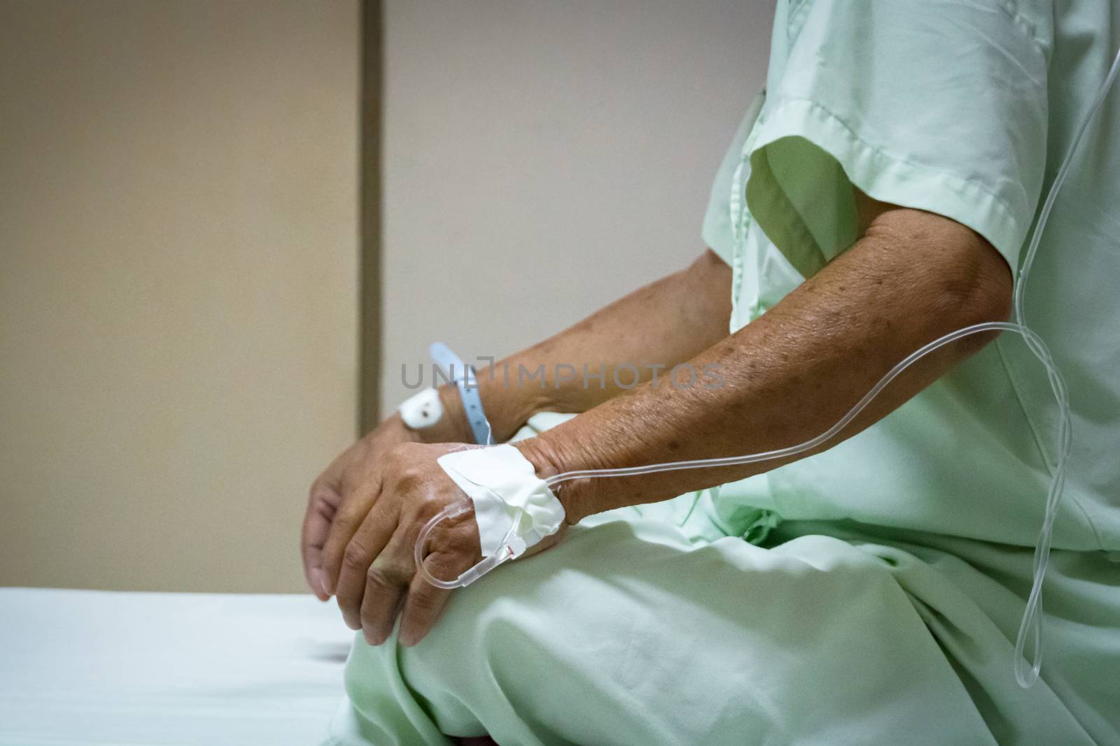 Patient asian elder man 70s with saline intravenous at C-line or A-line on a elderly patient hand on patient bed in intensive care unit (ICU.) room at hospital.