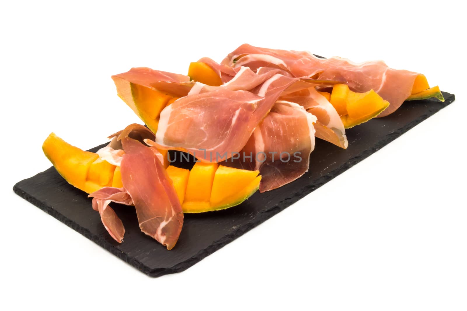 melon with ham placed on a rectangular slate plate on a white background
