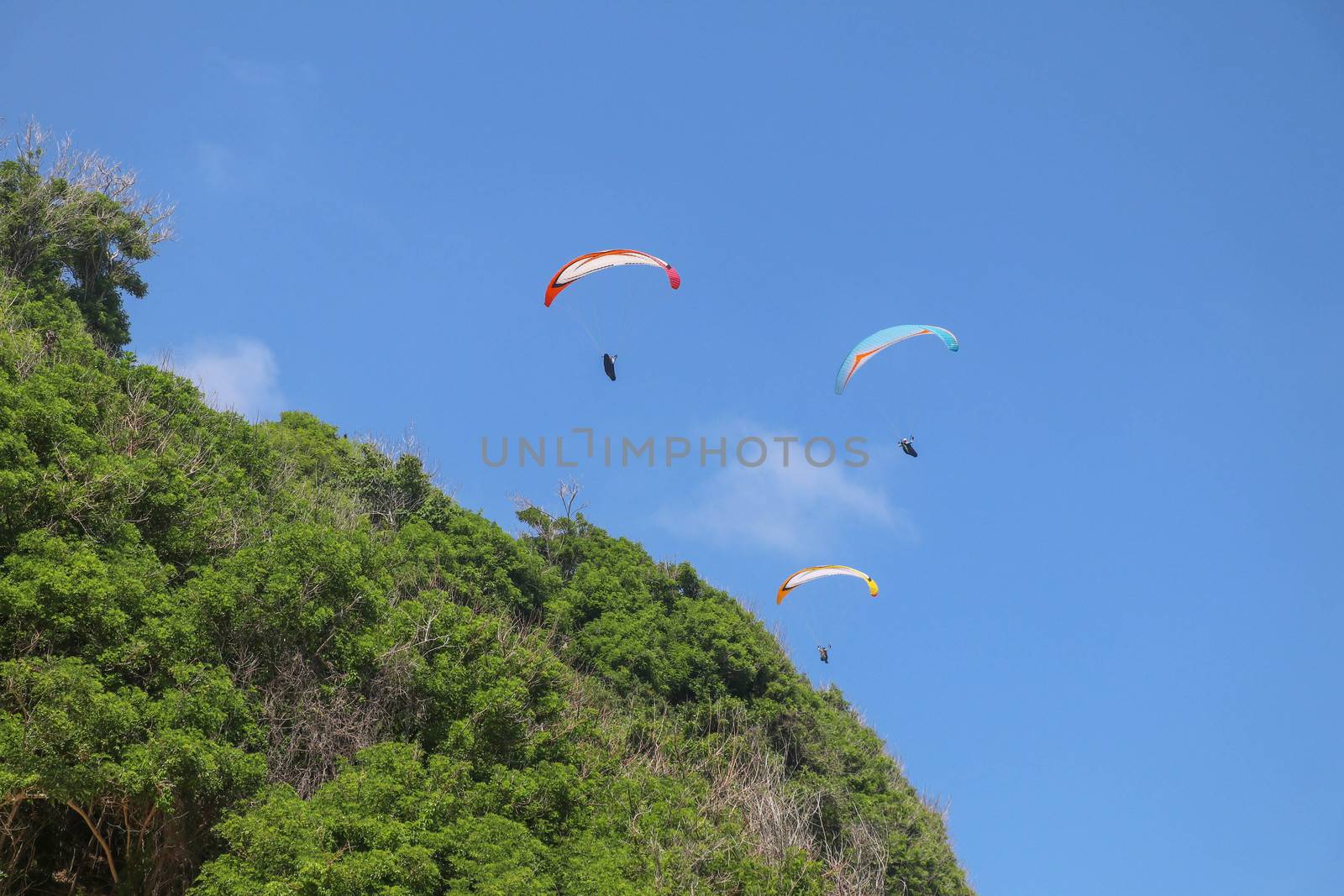 Paragliding in the sky. Three single paragliders flying in summer day over tropical Bali island. Beautiful paraglider in flight on a turquise background. Concept of active lifestyle and extreme sport.