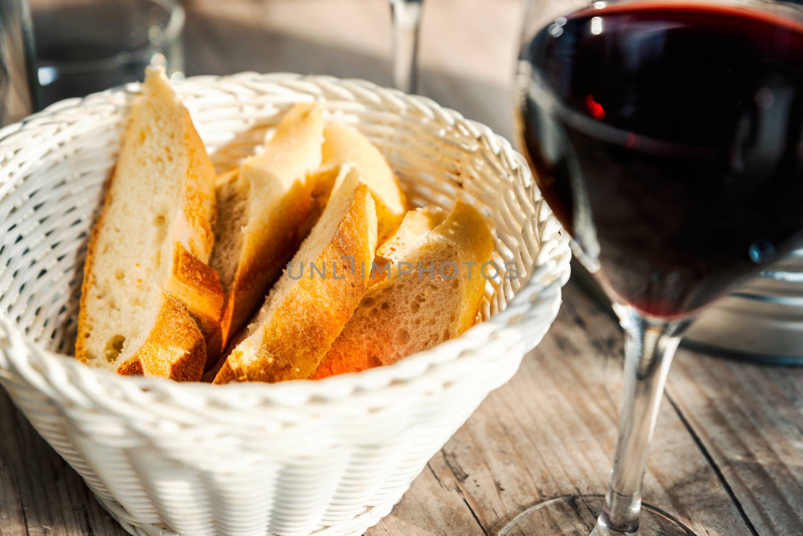 Baguette slices in basket and a glass of red wine by dutourdumonde