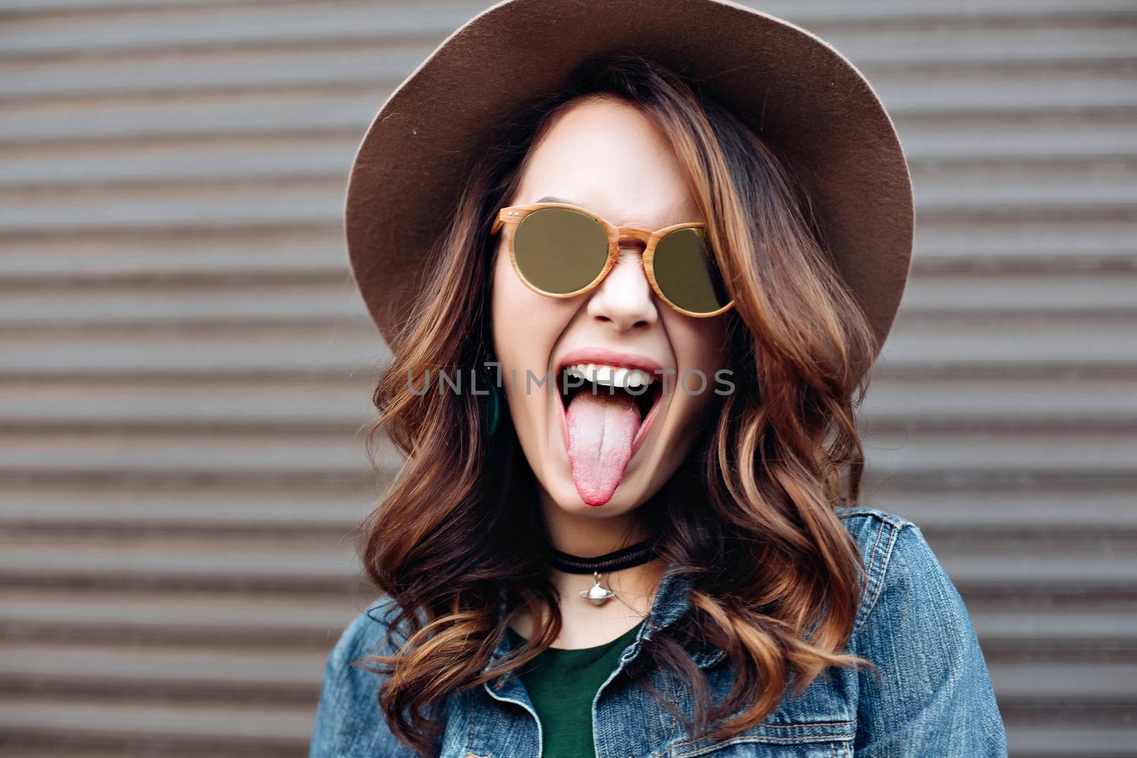 Happy beautiful brunette woman in sunglasses, striped white and black blouse smiling at camera, posing at camera. Gorgeous girl with perfect skin, plump lips, wavy hair. Walking at street. Sunset.