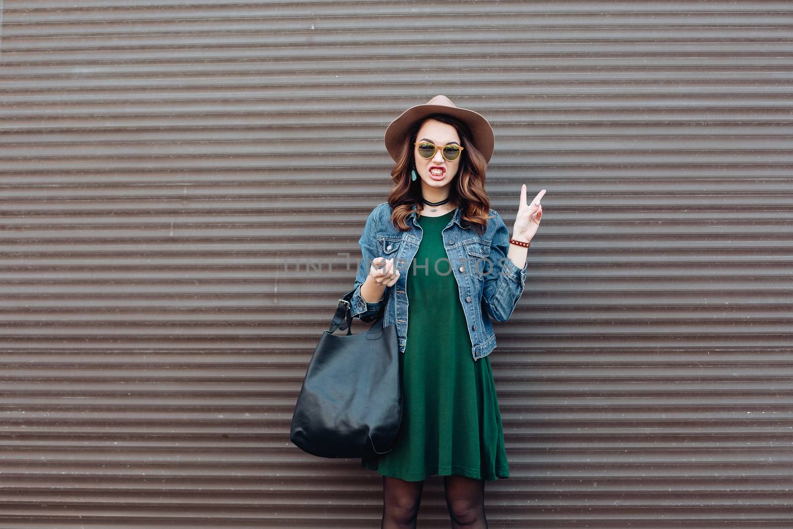 Fashionable brunette in brown hat, jeans jacket and choker on neck posing at street,looking at camera. Confident stylish woman with handbag, after beauty salon and shopping. Street swag style.
