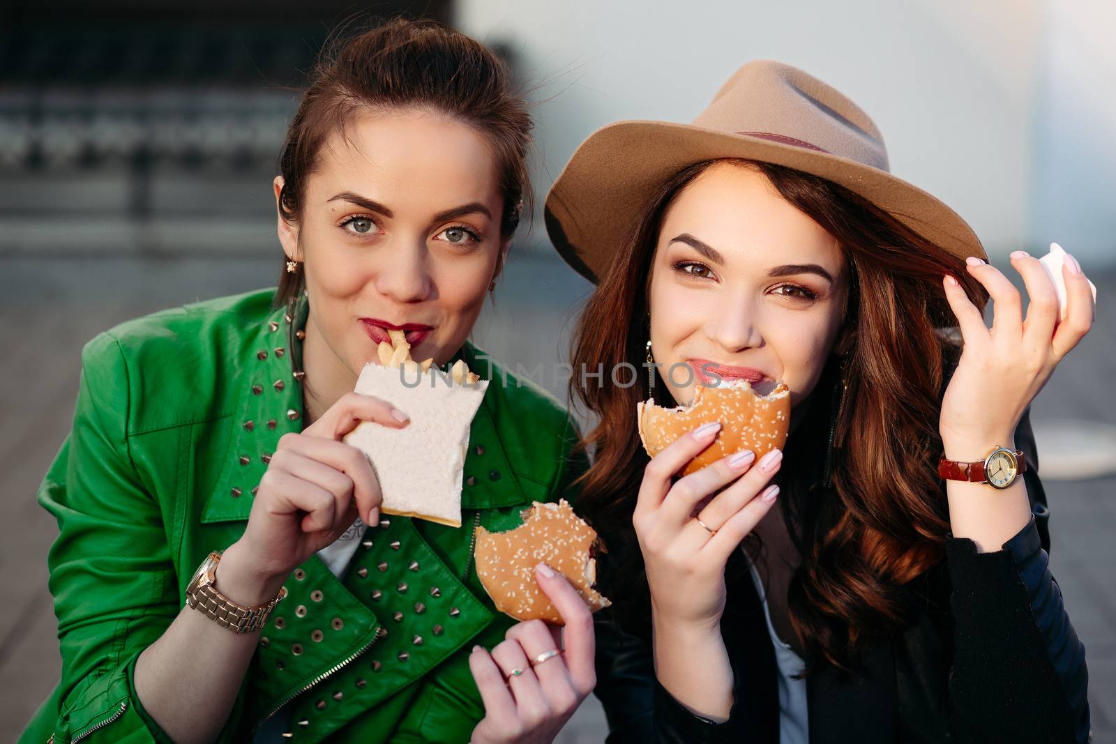 Funny girls eating hamburger and potato fried at street. by StudioLucky