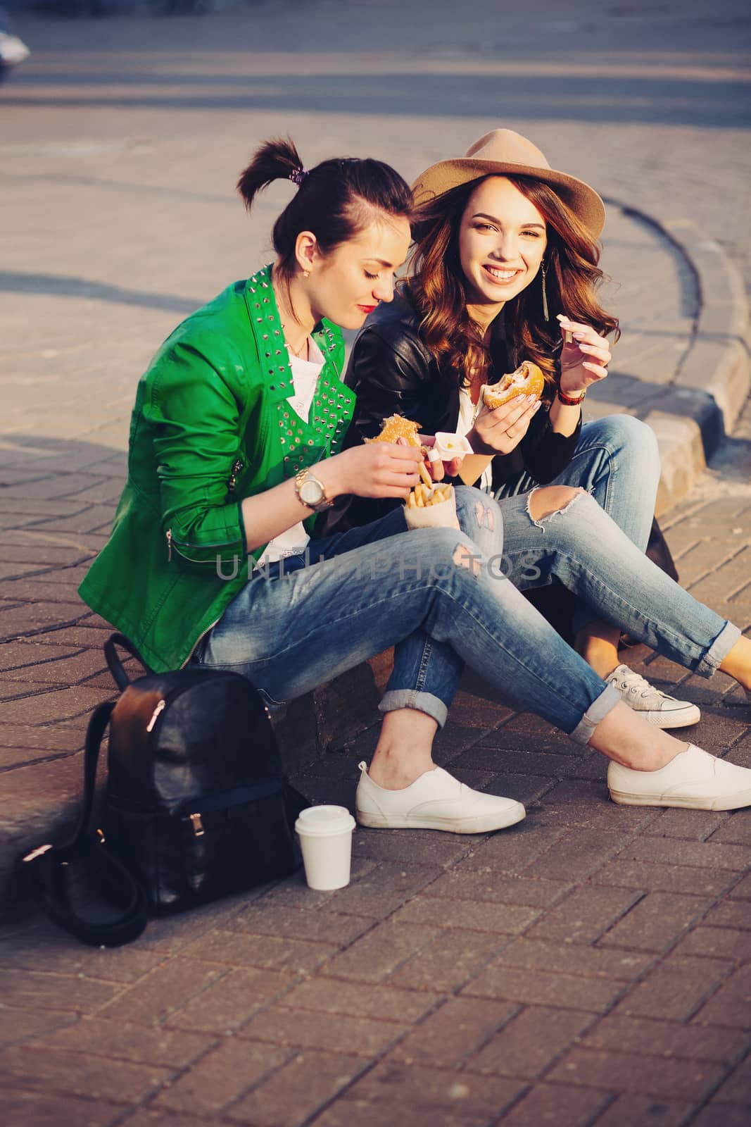 Funny girls eating hamburger and potato fried at street. by StudioLucky