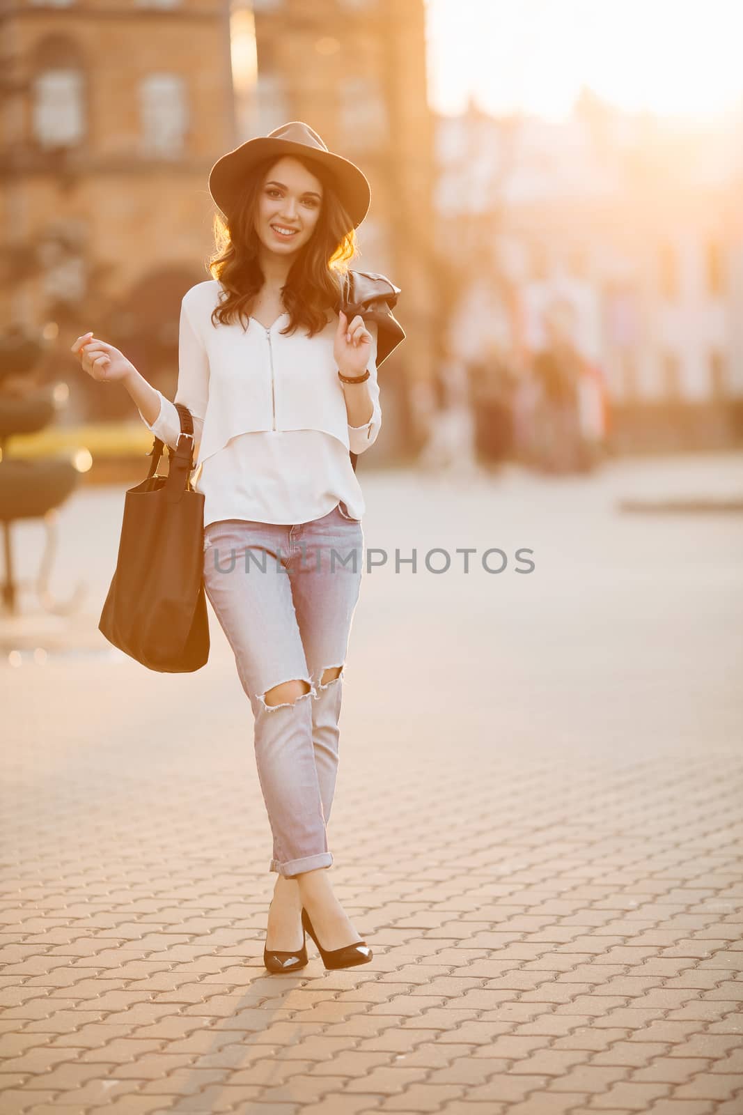 Brunette woman in hat walking at sunset after shopping. by StudioLucky