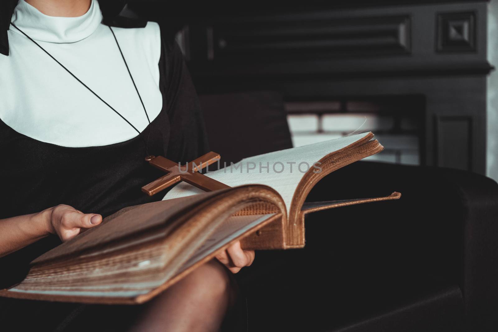 Nun in religion black suit holds Bible and posing on camera with big book on a black background. Close-up. Religion concept.