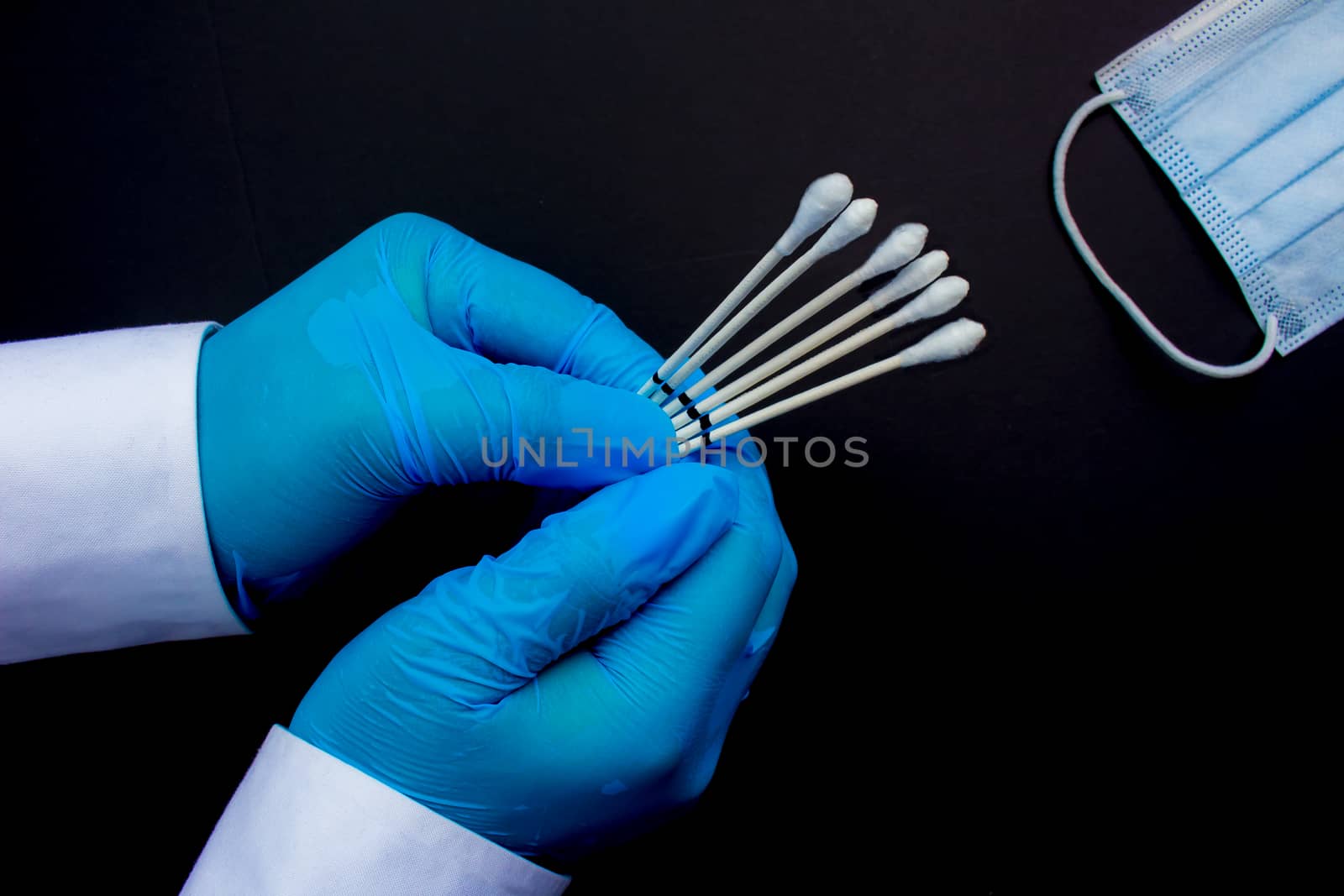 A medical personal holding throat swabs next to a medical face mask on a black background.
