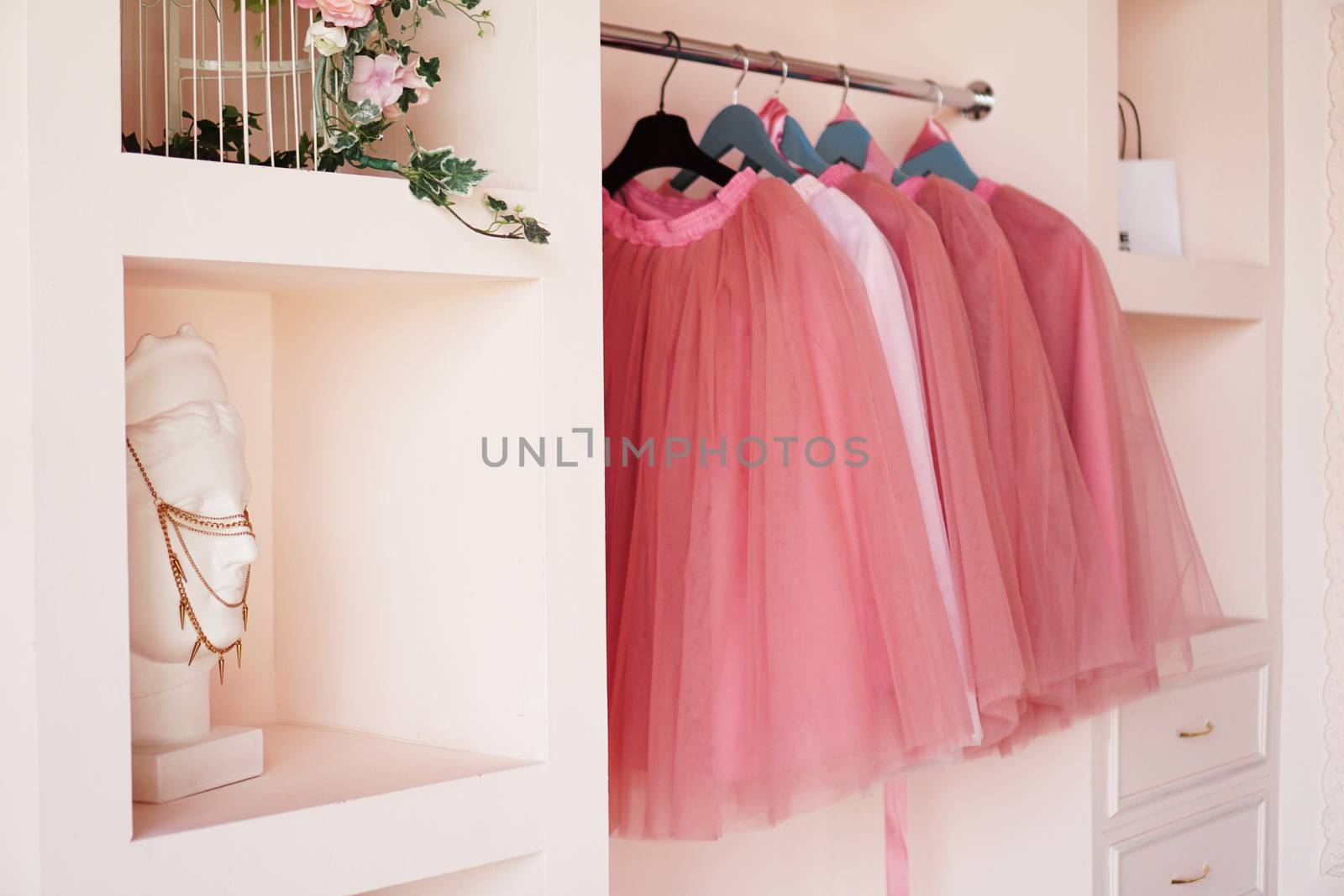 Dressing closet with pink clothes is arranged on hangers. The wardrobe is full of pink skirts, accessories on the shelves.