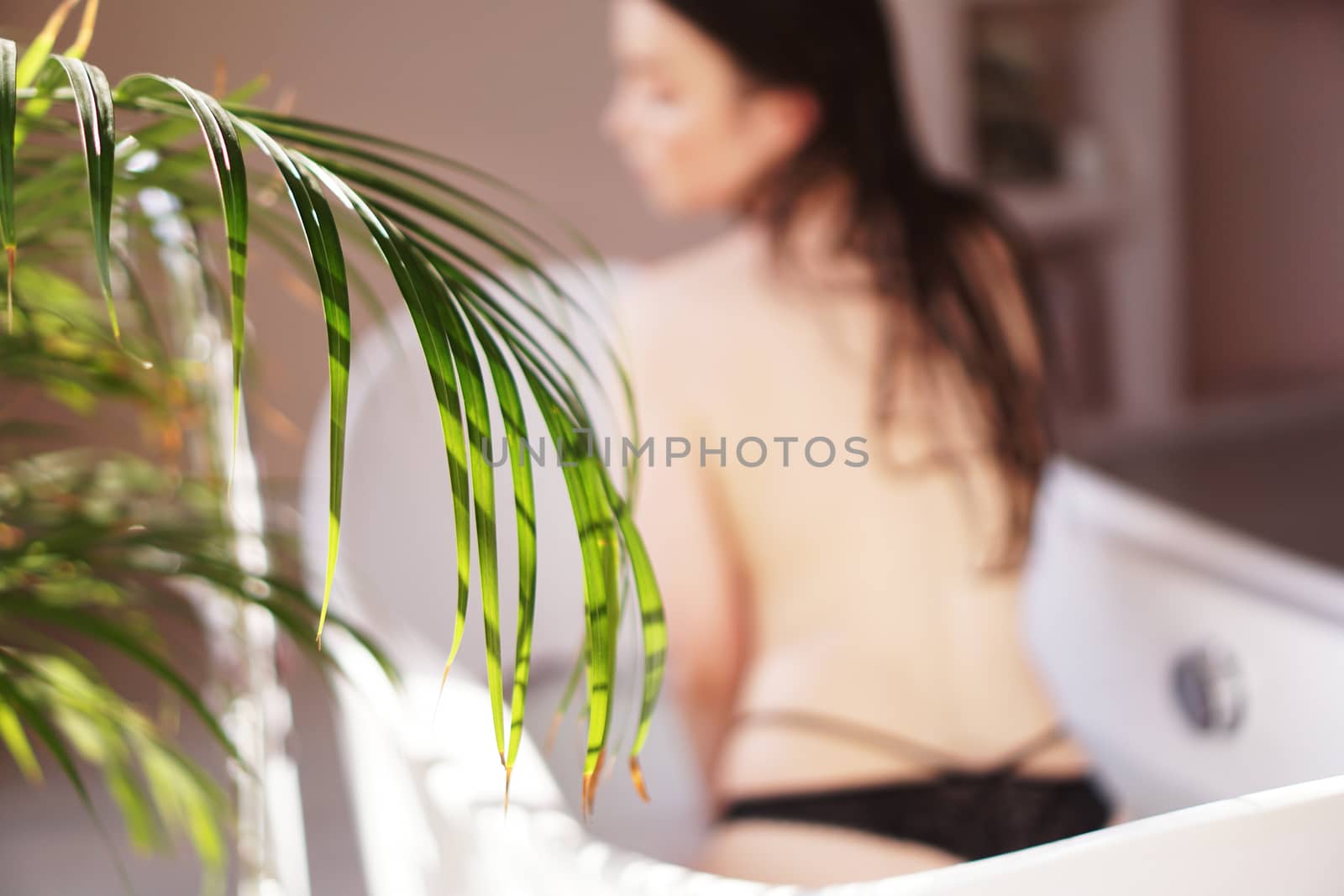 Pretty girl in bathroom - white bath. Green plant and blurred background
