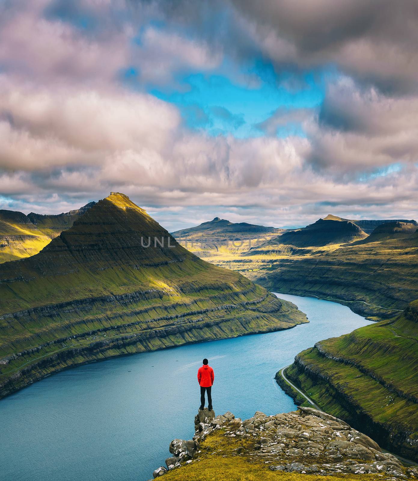 Hiker enjoys spectacular views over fjords from the summit of a mountain near Funningur on Faroe Islands.