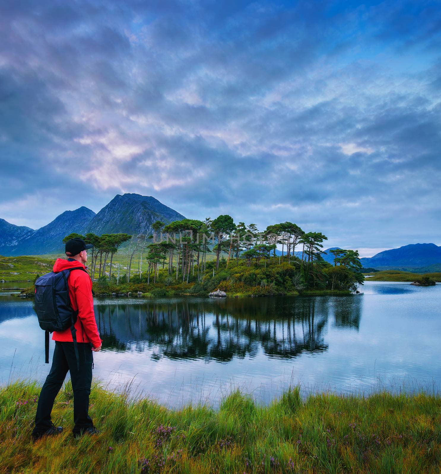 Young hiker with a backpack looking at the Pine Island in Derryclare Lough, Galway county, Ireland